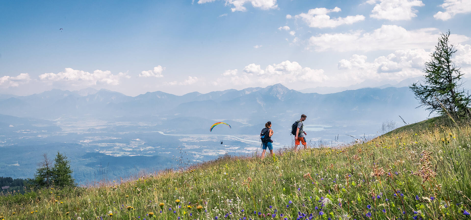 Pärchen beim Wandern auf der Gerlitzen Alpe mit Paragleiter im Hintergrund